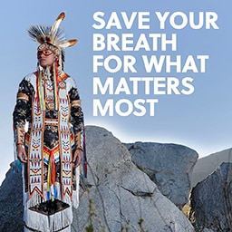 A person in Native American attire stands on a mountain with an anti-tobacco message.