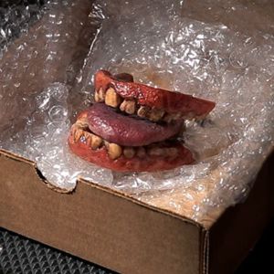 teeth and gums with a tongue inside an open cardboard box line with bubble wrap