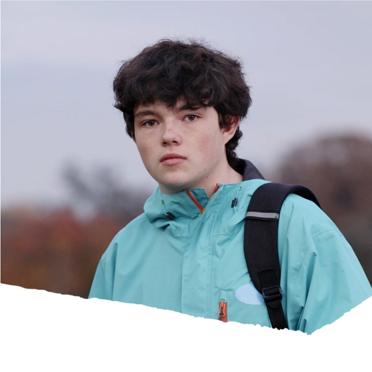 A native teen standing in a park on a gloomy day wearing a backpack.